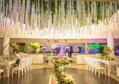 Salón de eventos decorado en blanco con techo vegetal, cintas colgantes, pista de baile y tarta nupcial.