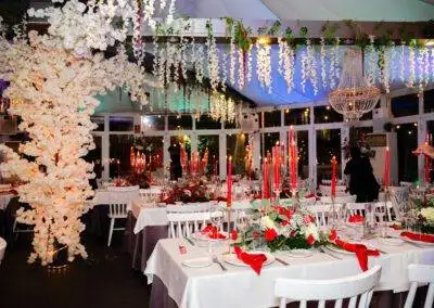 Vista general de salón de bodas decorado en rojo y blanco con árbol floral, flores colgantes y candelabros.