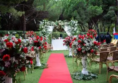 Pasillo de boda civil en jardín con alfombra roja, columnas blancas y arco floral de rosas rojas y blancas.